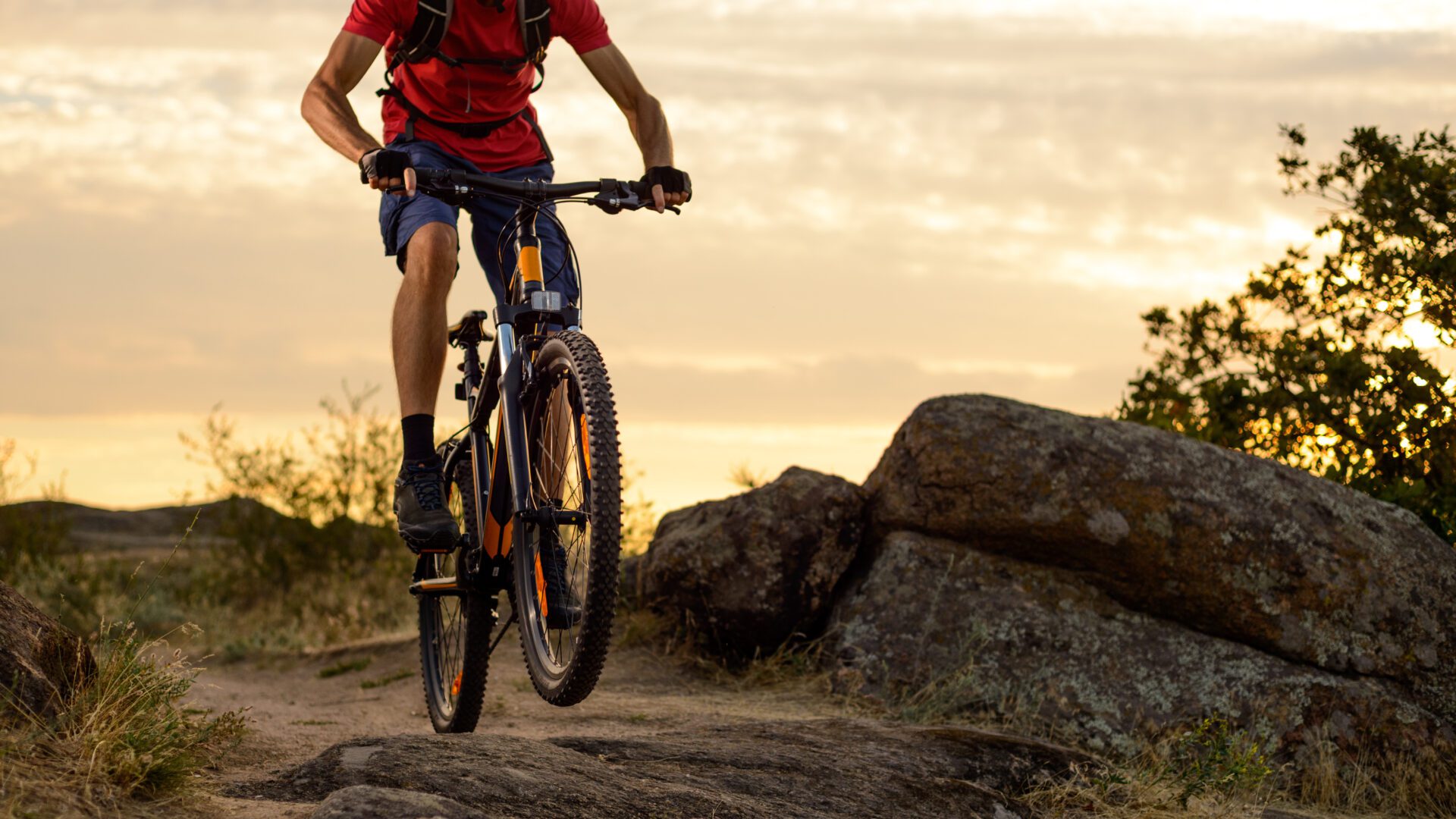 Cyclist in Red Riding the Bike on the Rocky Trail at Sunset. Extreme Sport and Enduro Biking Concept. snowboards skis kept together