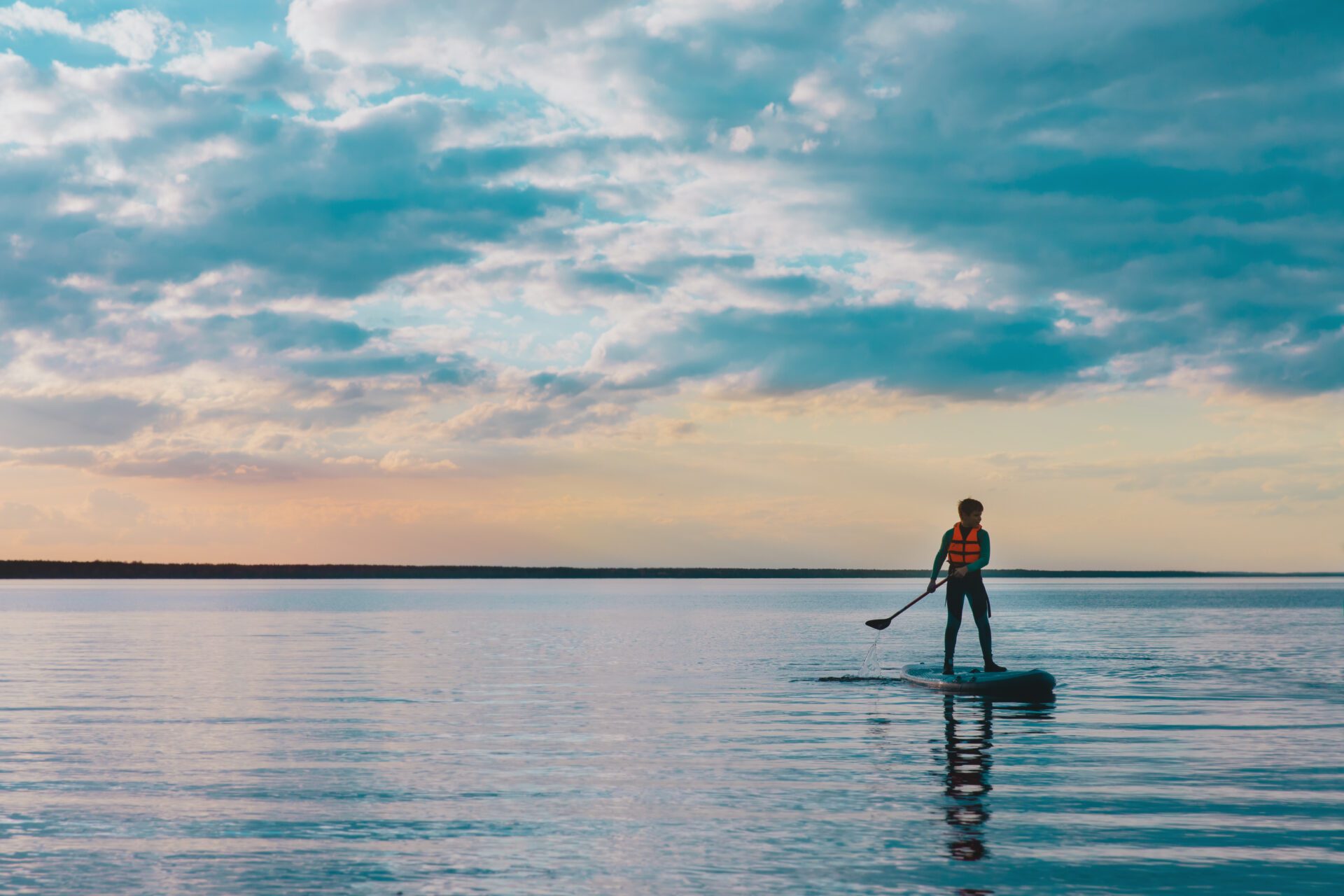 Kid riding on paddle sup surfboard in water at sunset group of people cycling on the road